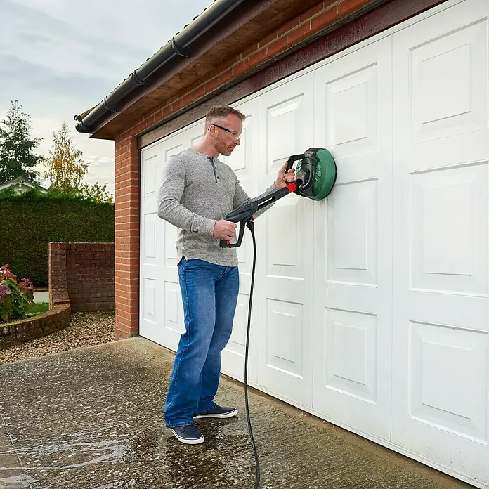 Bosch Flächenreiniger Multi Aquasurf 280 - Durchmesser: 280 mm, Passend für: Bosch Hochdruckreiniger Aquatak Serie - Ein Mann reinigt ein weißes Garagentor mit einem Bosch-Hochdruckreiniger und rotierender Bürste für eine gründliche Reinigung.