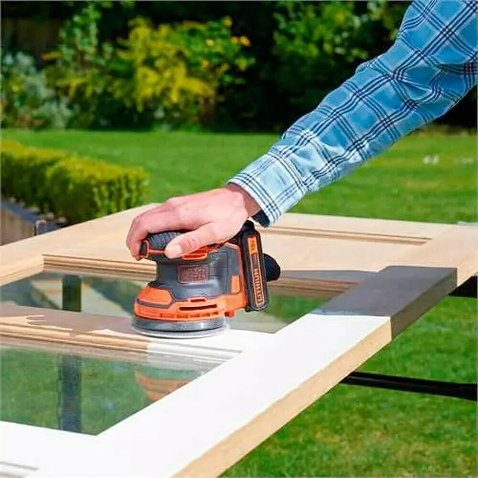 Black+Decker 18V PowerConnect Lijadora excéntrica de batería BDCROS18-QW - 18 V, Iones de litio, 1,5 Ah, 1 batería, 125 mm - Primer plano de una lijadora orbital inalámbrica de Black+Decker en acción, ideal para lijar superficies de madera con comodidad y precisión.