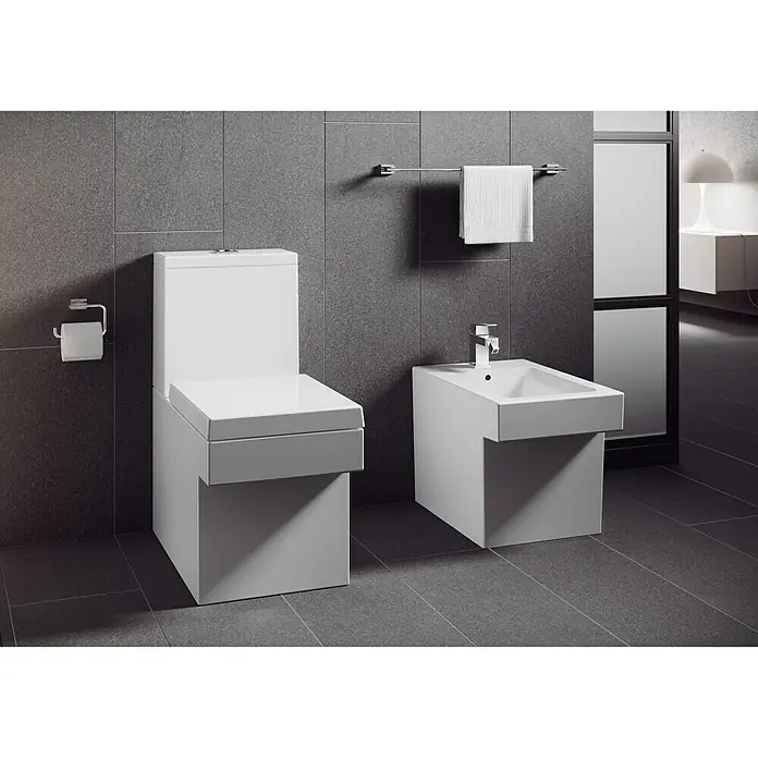 Grohe Essentials Cube Toilettenpapierhalter - Ohne Deckel, Chrom, Glänzend - Ein modernes Badezimmer mit einer quadratischen Toilette und einem Bidet in weiß, dazu Handtuchhalter und Toilettenpapierhalter an grauen Fliesen.