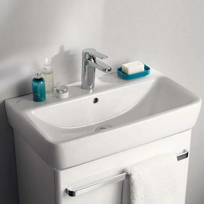 Geberit Renova Comprimo Waschtisch - 55 x 37 cm, Mit schmutzabweisender Glasur, Hahnloch: Mitte, Mit Überlauf, Weiß - Nahaufnahme eines weißen Badezimmerschranks mit Waschbecken, Armatur und Handtuchhalter. Elegantes und funktionales Design für moderne Badezimmer.
