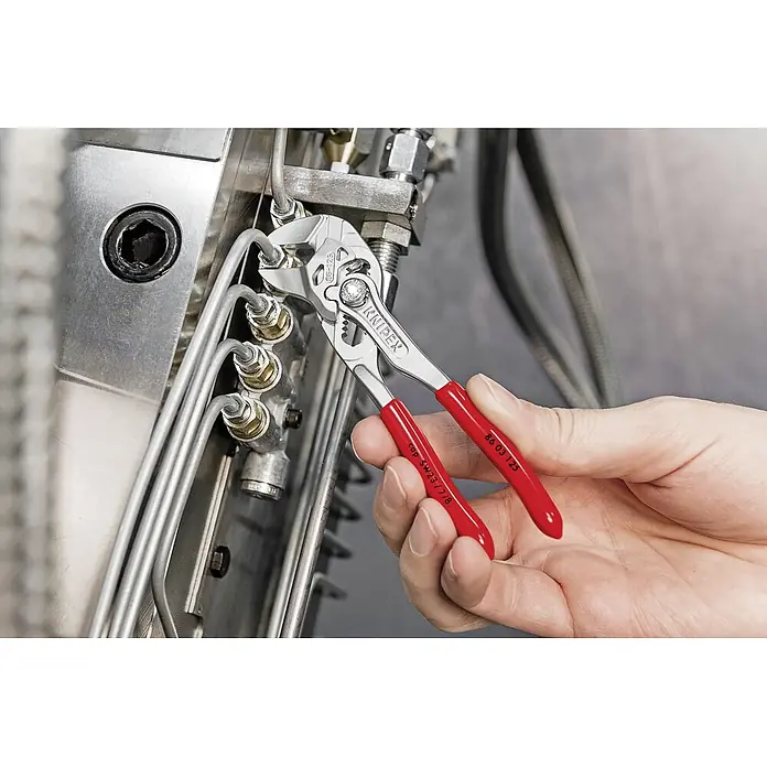 Knipex Wasserpumpenzange - Länge: 125 mm - Die Knipex Zange 86 03 125 wird verwendet, um eine Rohrverbindung an einer Maschine zu befestigen. Rote Griffe sind sichtbar.