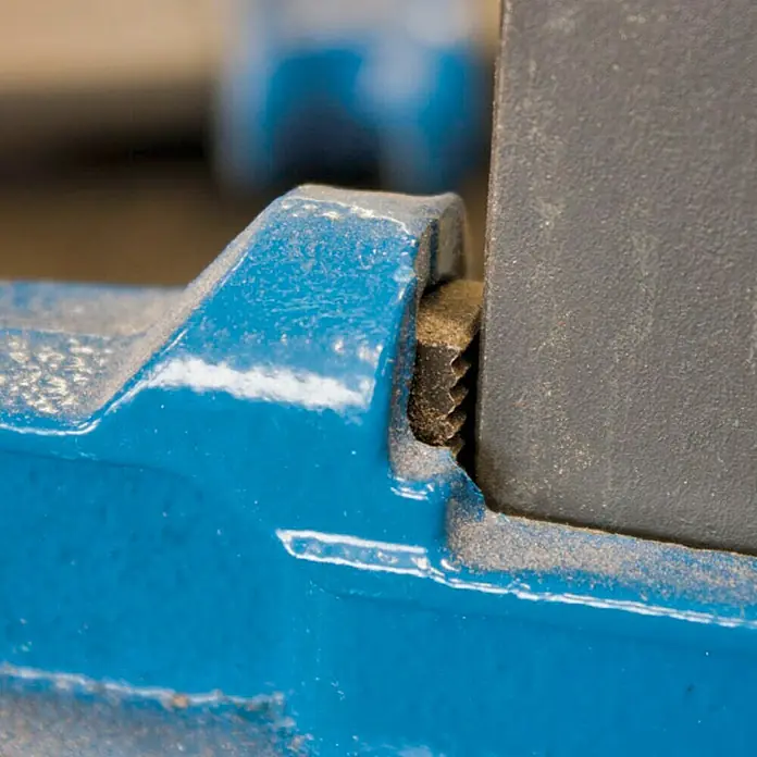 Piher Sargento F-40 - Anchura de sujeción: 400 mm, Fuerza de tensión: 9.000 N, Apertura máxima: 120 mm - Detalle de una abrazadera de tornillo azul con rosca gruesa, asegurando una pieza de trabajo gris. Primer plano de la herramienta en acción.