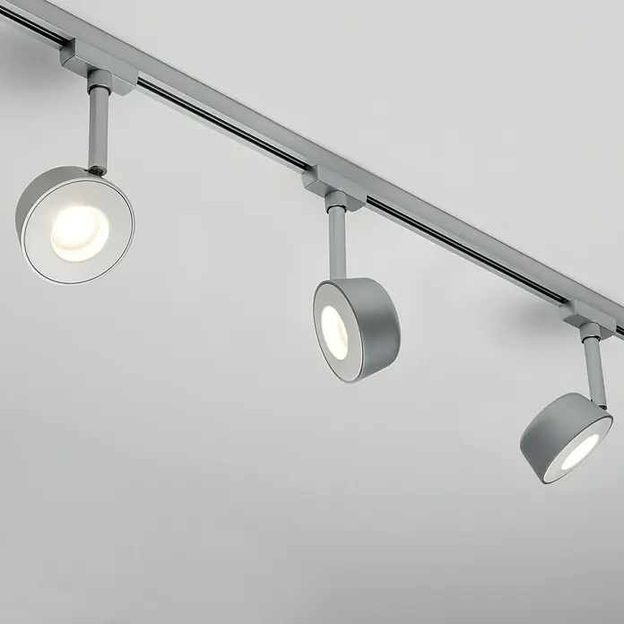 Paulmann URail LED-Spot Pellet - 4 W, Lichtfarbe: Warmweiß - Nahaufnahme von drei grauen LED-Strahlern an einer Schiene an einer weißen Decke, die moderne Beleuchtungslösungen hervorheben.