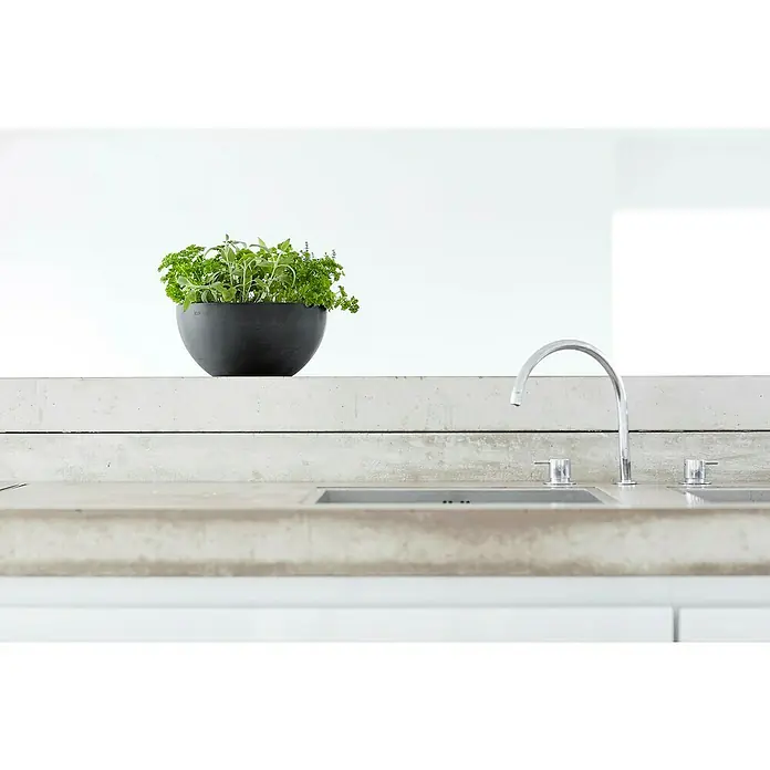 Ecopots Brussels Pflanzschale rund - Außenmaß (Ø x H): 25 x 12 cm, Kunststoff, Dunkelgrau - Küchentisch mit Kräutertopf in einer schwarzen Schale und einer modernen Armatur. Die Arbeitsplatte besteht aus Beton.