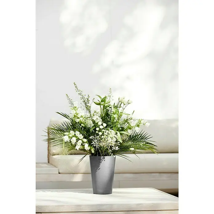 Ecopots Vase Pisa - Ø x H: 17,8 x 25,2 cm, Kunststoff, Grau - Ein Arrangement aus weißen Blumen und grünem Blattwerk in einer stilvollen, grauen Vase, die auf einem Tisch vor einem hellen Hintergrund steht.