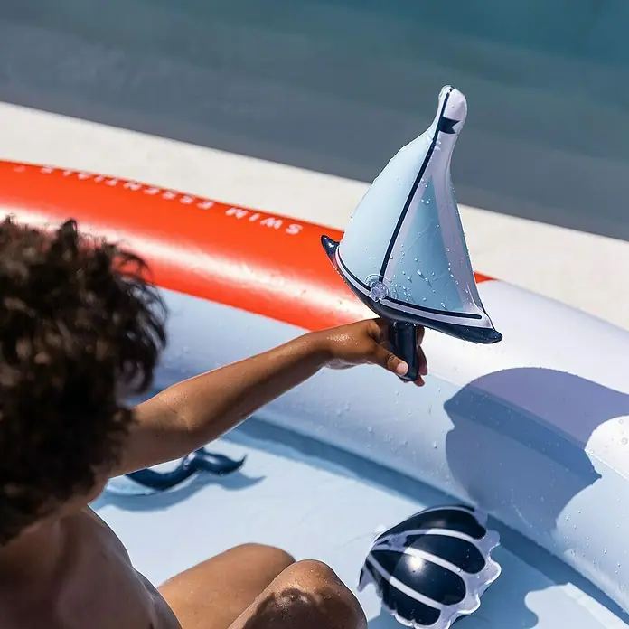 Swim Essentials Planschbecken Whale - Ø x H: 210 x 150 cm - Ein Kind spielt im Pool mit einem aufblasbaren Spielzeugboot mit weißen und blauen Segeln. Das Boot ist das Hauptaugenmerk des Bildes.