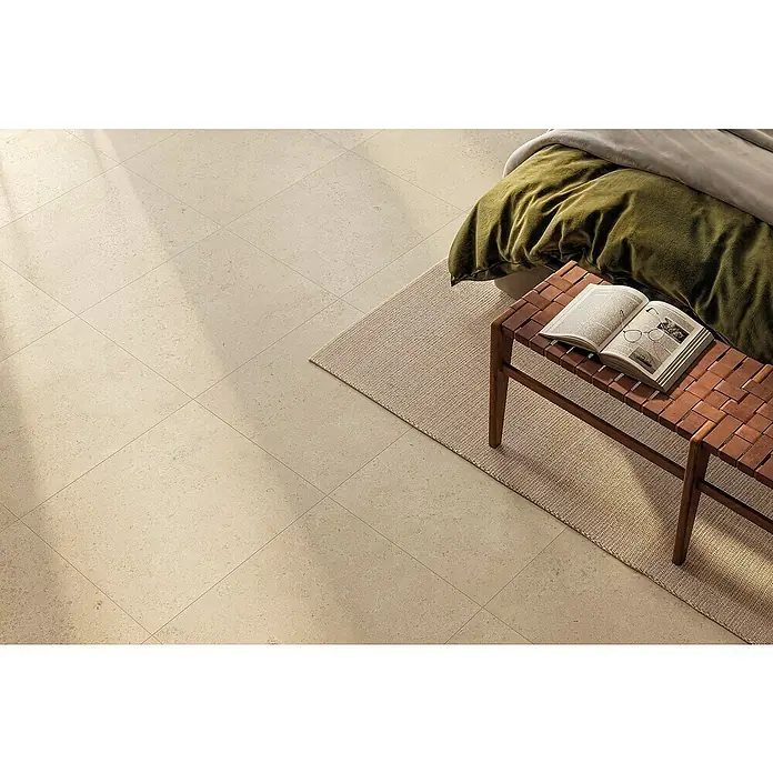 Atlas Concorde Solution Feinsteinzeugfliese Lunastone - 60 x 60 cm, Sand, Matt - Beiges Feinsteinzeugfliesen-Interieur mit gefliester Oberfläche, ergänzt durch Teppich und Fußhocker mit Buch.