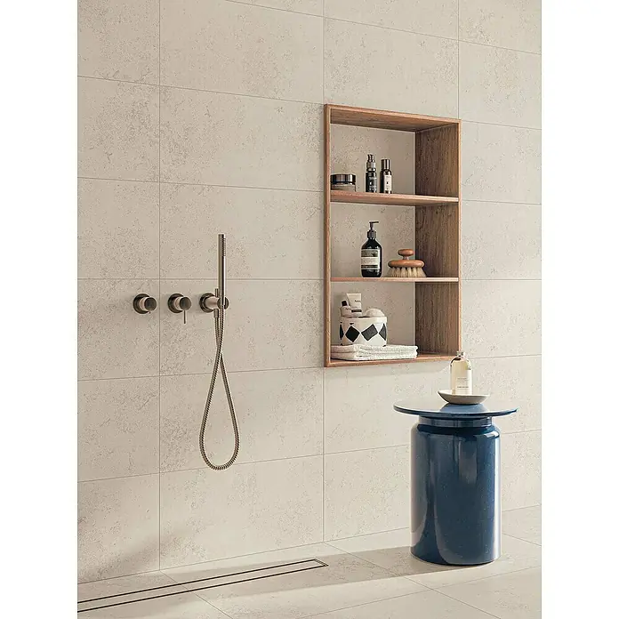 Atlas Concorde Solution Feinsteinzeugfliese Lunastone - 30 x 60 cm, Ivory, Matt - Elegantes Badezimmerdesign mit einem stilvollen, blauen Hocker und einer praktischen Wandnische zur Aufbewahrung von Badutensilien.