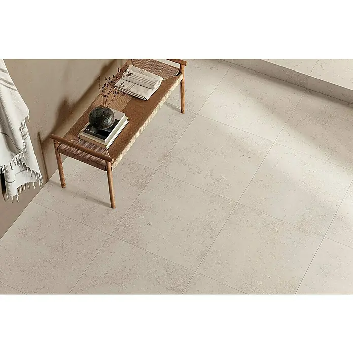 Atlas Concorde Solution Feinsteinzeugfliese Lunastone - 60 x 60 cm, Ivory, Matt - Nahaufnahme von Bodenfliesen in einem Badezimmer mit einer Holzbank, Handtüchern und Dekorationsgegenständen.