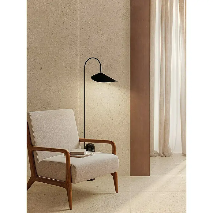 Atlas Concorde Solution Feinsteinzeugfliese Lunastone - 30 x 60 cm, Sand, Matt - Elegantes Interieur mit beigem Sessel, Stehlampe und dezenten Vorhängen vor einer strukturierten Wand, das ein modernes und stilvolles Wohnambiente präsentiert.