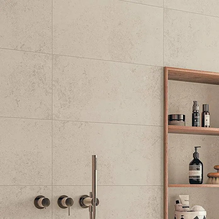 Atlas Concorde Solution Feinsteinzeugfliese Lunastone - 30 x 60 cm, Ivory, Matt - Nahaufnahme einer gefliesten Wand im Badezimmer mit Armaturen und einem Holzregal mit Pflegeprodukten.