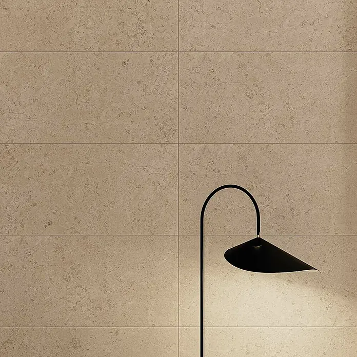 Atlas Concorde Solution Feinsteinzeugfliese Lunastone - 30 x 60 cm, Sand, Matt - Nahaufnahme einer beigen Wandfliese mit einer schlanken, schwarzen Stehlampe. Das Licht betont die Textur der Fliese.