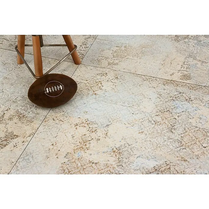 Feinsteinzeugfliese Carpet Natural - 100 x 100 cm, Sand, Matt - Ein brauner Football liegt unter einem Hocker auf gemusterten Fliesen. Das Sportgerät ist detailreich mit weißen Nähten versehen.