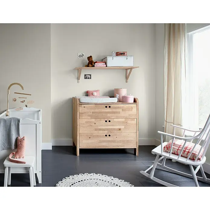 Bruguer Elegance Pintura para paredes - Blanco niebla, Mate, 4 l - Un cuarto infantil brillante con una cómoda de madera con detalles de estrellas, una cuna blanca y una mecedora.
