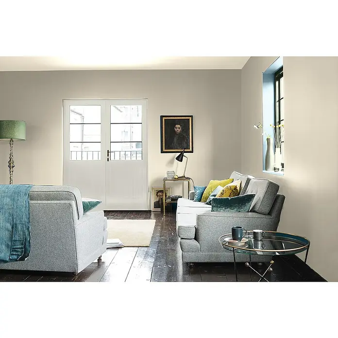 Bruguer Elegance Pintura para paredes - Blanco elegante, Mate, 4 l - Acogedora sala de estar con sofá gris, sillón y mesa auxiliar. Diseño interior elegante con colores suaves y luz natural para un ambiente acogedor.