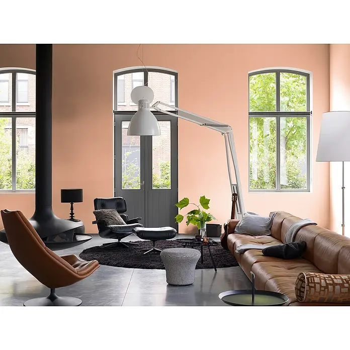 Bruguer Elegance Pintura para paredes - Terracota rústica, Mate, 4 l - Salón luminoso con sofá de cuero marrón, chimenea independiente y grandes ventanales. El espacio irradia calidez y confort.