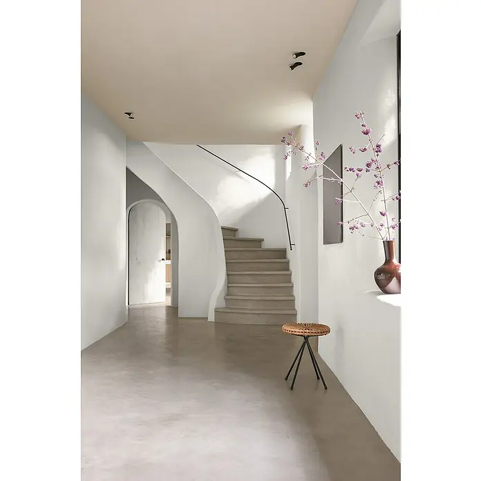 Bruguer Elegance Pintura para paredes - Blanco piedra, Mate, 4 l - Escalera beige con barandilla negra. Un taburete decorativo y un jarrón con flores rosas acentúan la estancia y crean un ambiente acogedor.