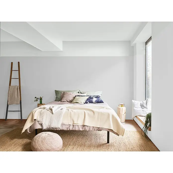 Bruguer Elegance Pintura para paredes - Gris brisa, Mate, 4 l - Decoración luminosa de dormitorio con cama, escalera y puf de mimbre sobre una alfombra. La luz natural entra por la ventana.