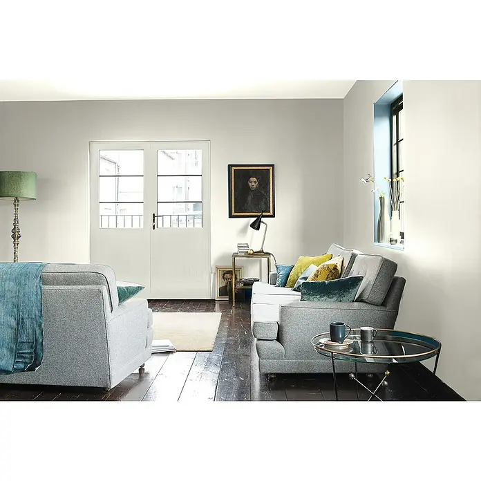 Bruguer Elegance Pintura para paredes - Beige arena, Mate, 4 l - Una acogedora sala de estar con sofás y sillones grises, una mesa redonda y arte en la pared. Ambiente luminoso y acogedor.