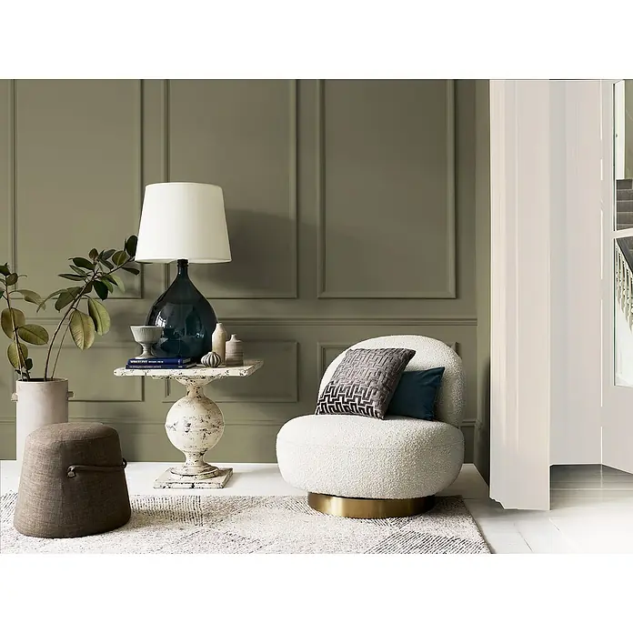 Bruguer Elegance Pintura para paredes - Verde oliva, Mate, 4 l - Interior elegante con sillón bouclé, lámpara de mesa y mesa auxiliar. La combinación crea un ambiente acogedor y elegante en la habitación.