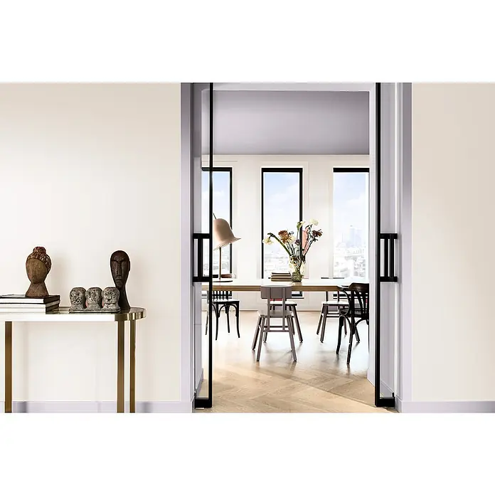 Bruguer Elegance Pintura para paredes - Blanco roto, Mate, 4 l - Vista a través de una puerta abierta, que muestra una mesa de comedor minimalista y arte decorativo en una consola dorada.