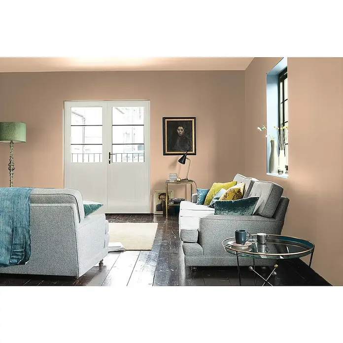 Bruguer Elegance Pintura para paredes - Camel clásico, Mate, 4 l - Una sala de estar acogedora con sofá gris claro, sillón y mesa de vidrio. Las paredes están pintadas en un tono melocotón cálido, creando un ambiente acogedor.