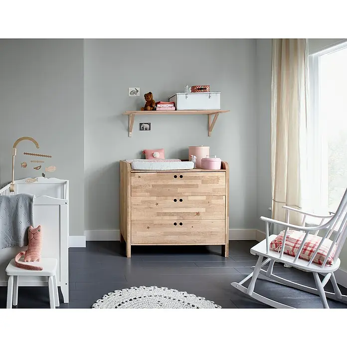 Bruguer Elegance Pintura para paredes - Gris piedra, Mate, 4 l - Habitación infantil con una mesa para cambiar pañales de madera clara adornada con estrellas, acompañada de una cuna blanca y mecedora.