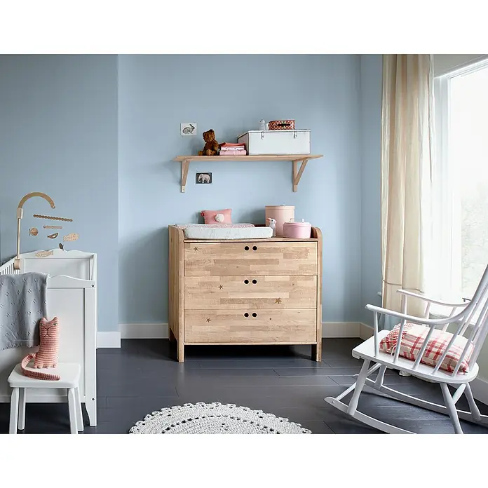 Bruguer Elegance Pintura para paredes - Azul bruma, Mate, 4 l - La luminosa habitación del bebé cuenta con una cómoda de madera de tres cajones, una cuna y una mecedora para un ambiente acogedor.