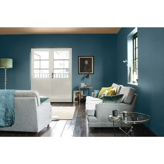 Bruguer Elegance Pintura para paredes - Azul naval, Mate, 4 l - Un elegante salón con sofás grises, una mesa redonda y una alfombra sobre suelos de madera oscura, todo complementado por elegantes paredes azules.