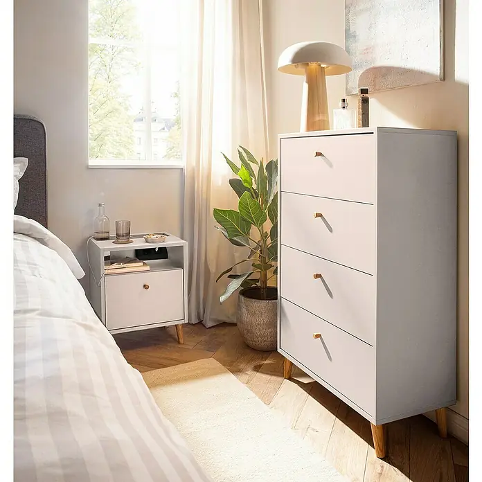 Schildmeyer Bjarne Kommode - L x B x H: 33 x 60 x 101,3 cm, Weiß, Anzahl Schubladen: 4 Stk. - Das Bild zeigt eine weiße Kommode mit vier Schubladen und hölzernen Füßen in einem hellen Schlafzimmer neben einem Nachttisch.