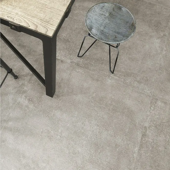 Feinsteinzeugfliese Savanna - 59,7 x 59,7 cm, Desert, Matt - Nahaufnahme eines Tisches und eines Hockers auf einem Fliesenboden, der die Textur und das Design des Bodens hervorhebt.