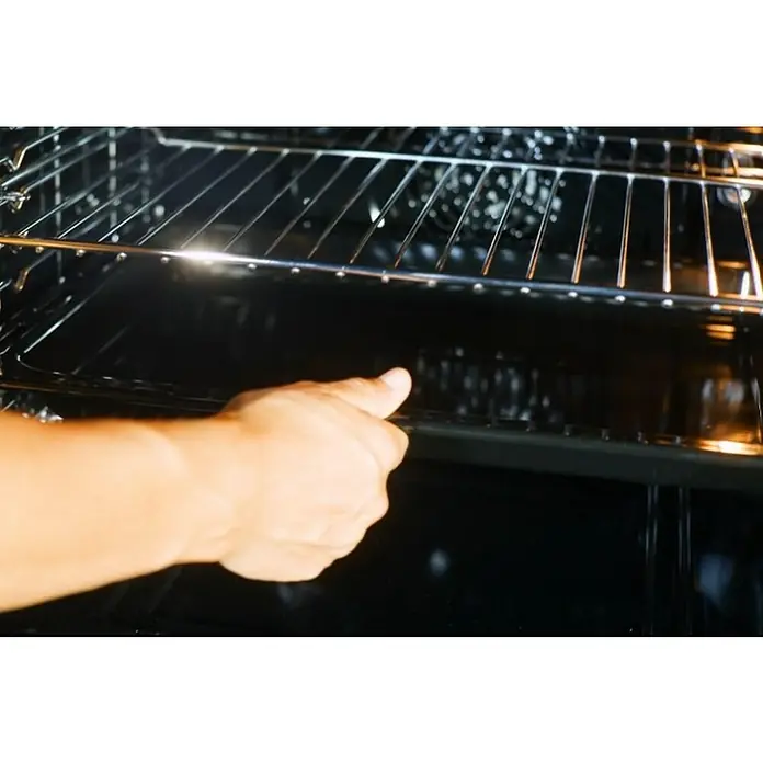 Corberó Horno empotrado CCHMD805N - Volumen horno: 70 l - Una persona con un brazo colocando una bandeja negra en el horno con rejillas. Para una distribución uniforme del calor.