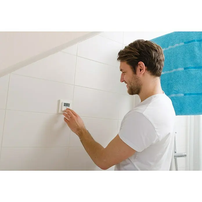 Homematic IP Funk-Raumthermostat HmIP-BWTH - Netzbetrieben, 230 V, 54 x 86 x 86 mm, Weiß - Mann stellt elektronischen Thermostat an der Badezimmerwand ein, um die Temperatur zu regulieren.