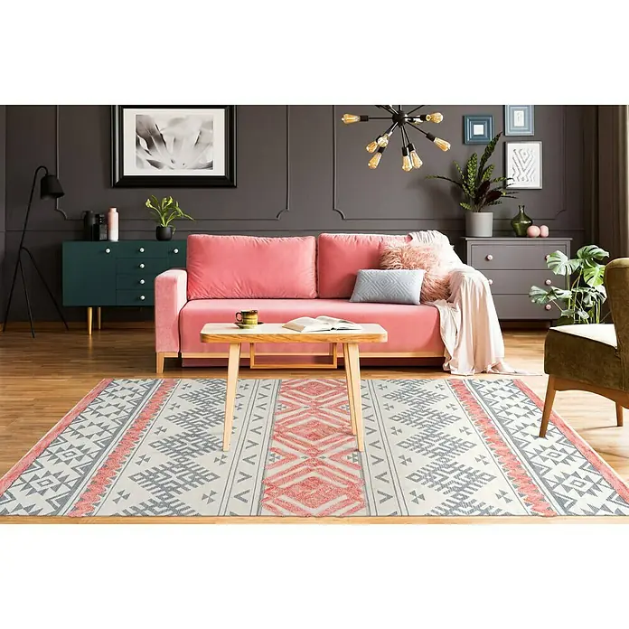 Kayoom Flachgewebeteppich Ethnie - Grau/Rot, 230 x 160 cm, 100 % Baumwolle - Ein stilvoller Wohnraum mit einem geometrischen Teppich, einem rosa Sofa und passenden Möbeln, die eine gemütliche Atmosphäre schaffen.