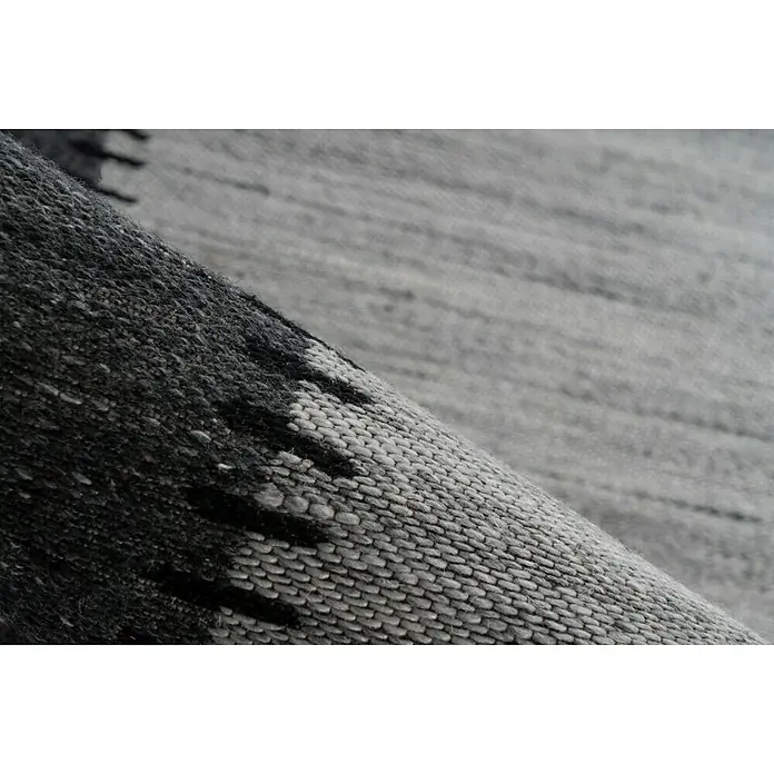 Kayoom Flachgewebeteppich Phoenix - Grau/Anthrazit, 170 x 120 cm, 75 % Wolle - Detailaufnahme eines grauen Teppichs mit dunklen Akzenten, der eine raffinierte Textur und ein dezentes Muster aufweist.