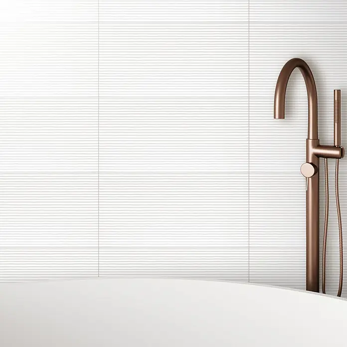 DryTile Wandfliese Palazzo Strukturiert Linie - 30 x 60 cm, Weiß, Matt - Elegante Badewanne mit Armatur in Kupferoptik vor einer stilvollen, weißen, horizontal geriffelten Wand, die dem Raum eine moderne Note verleiht.