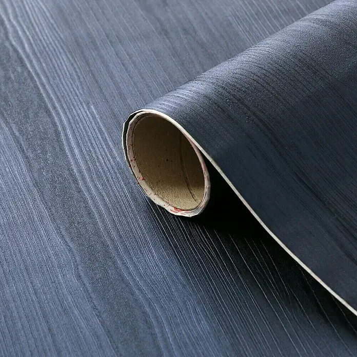 D-c-fix Lámina efecto madera Quadro - 150 x 67,5 cm, Azul noche, Autoadhesivo - Primer plano de un rollo de film de veta de madera oscura parcialmente desenrollado que revela el soporte de papel.