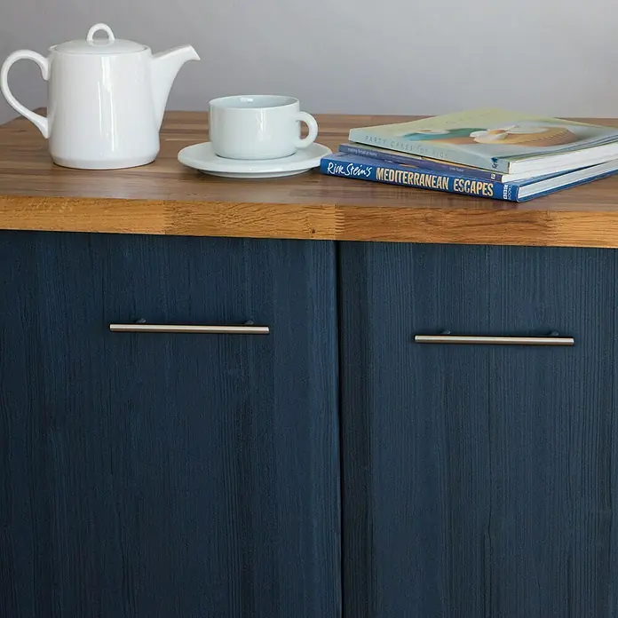 D-c-fix Lámina efecto madera Quadro - 150 x 67,5 cm, Azul noche, Autoadhesivo - Tetera, taza y libros expuestos en un aparador con puertas de armario pintadas de azul y tiradores plateados.