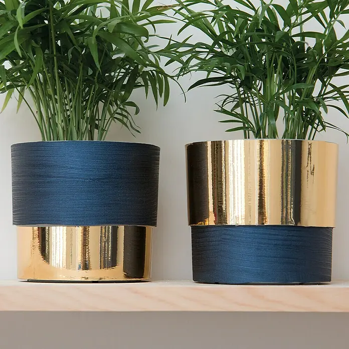 D-c-fix Lámina efecto madera Quadro - 150 x 67,5 cm, Azul noche, Autoadhesivo - Dos plantas de interior en macetas azules y doradas reposan sobre una estantería. Las macetas tienen un diseño moderno y elegante con líneas horizontales.