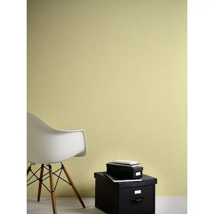 A.S. Création Vliestapete - Gelb, Uni, 10,05 x 0,53 m - Einrichten mit Stil: Ein weißer Stuhl und schwarze Aufbewahrungsboxen vor einer sanft gelben Wand schaffen eine minimalistische Atmosphäre.