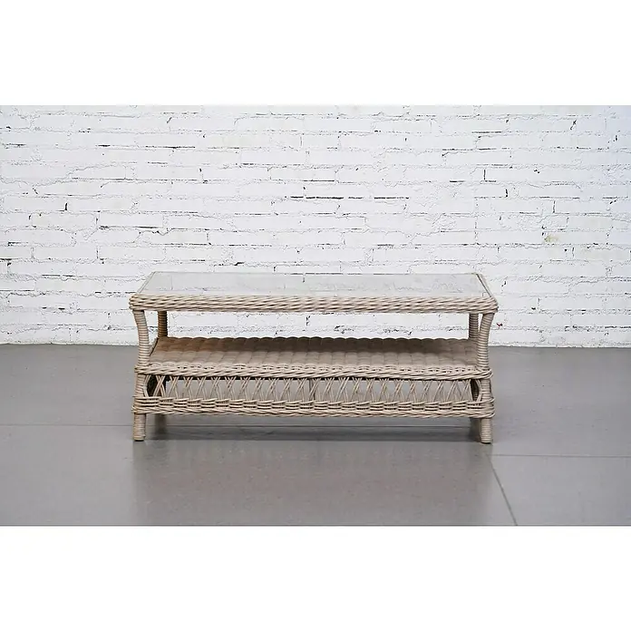 Sunfun Conjunto de muebles Soraya - 4 pzs., Ratán sintético/Aluminio/Poliéster, Beige/Gris - Una mesa de ratán beige con tapa de vidrio y estante frente a una pared de ladrillos blanca.