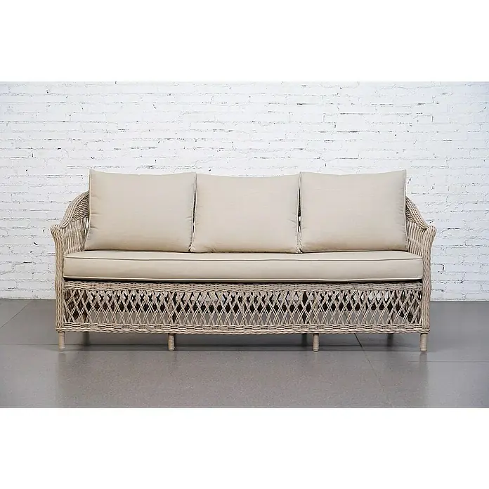 Sunfun Conjunto de muebles Soraya - 4 pzs., Ratán sintético/Aluminio/Poliéster, Beige/Gris - Elegante sofá de ratán con cojines beige frente a una pared de ladrillos blanca. El sofá ofrece una opción de asiento cómoda y elegante.