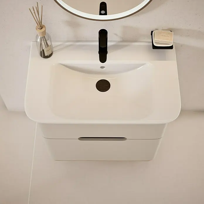 VitrA Sento Badmöbel-Set Sento - 80 cm, Hellgrau, 2 Schubladen - Nahaufnahme eines modernen Waschbeckens mit Unterschrank, Armatur, Seife und Duftstäbchen vor einem Spiegel.