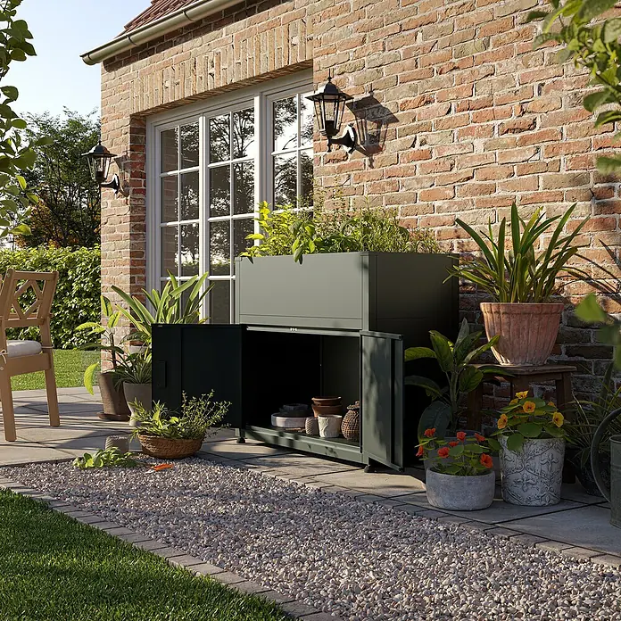 KGT Hochbeet UrbanGrow M Space - 101 x 51 x 86 cm, Metall, Anthrazit-grau - Das Bild zeigt einen stilvollen Pflanzkasten mit integriertem Stauraum vor einer Backsteinmauer, ideal für Gartenliebhaber.