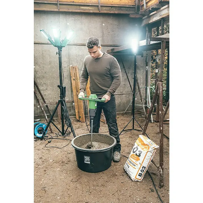 Berg Handrührwerk MX 19 - 1.850 W, Mischvolumen: 200 l - Ein Mann mischt Beton in einem Eimer mit einem grünen Mörtelrührer. Eine Packung Betonmischung lehnt an dem Eimer.