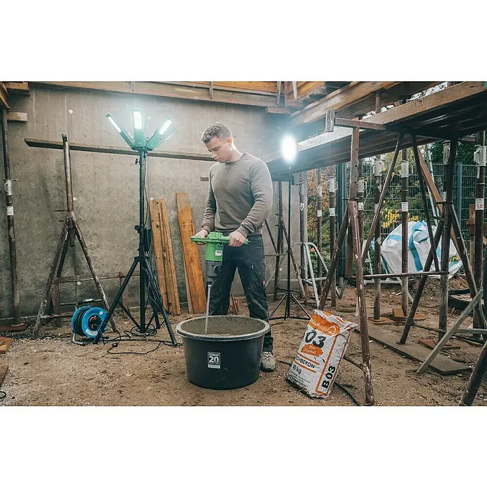 Berg Handrührwerk MX 19 - 1.850 W, Mischvolumen: 200 l - Mann mischt Beton mit einer Bohrmaschine in einem Eimer, umgeben von Baugeräten und einer Lampe.