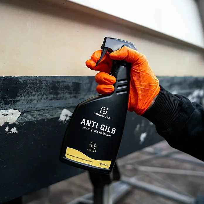 Sprenger Gelcoat Reiniger Anti Gilb - 500 ml - Eine Hand mit orangefarbenem Handschuh hält eine SPRINGER Anti Gilb Reinigungsflasche vor einem Gelcoat.
