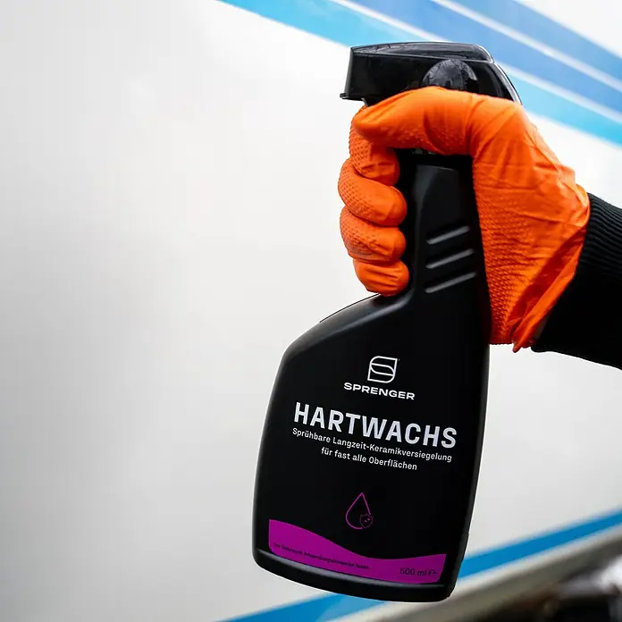 Sprenger Hartwachs-Politur - 500 ml - Sprühflasche mit Sprenger Hartwachs Langzeit-Keramikversiegelung für Oberflächen, gehalten von einer Hand mit orangefarbenem Handschuh.