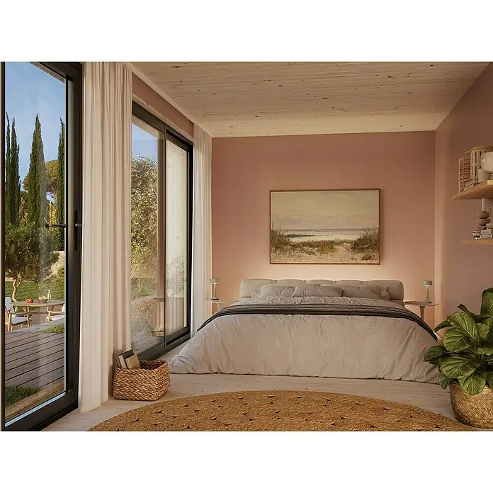 Palmako Gartenhaus Johanna Nordic Plus - Außenmaß inkl. Dachüberstand (B x T): 562 x 339 cm, Holz, Natur unbehandelt - Schlafzimmer mit Doppelbett, rundem Teppich, großen Fenstern und Blick ins Grüne. Dekoriert mit Pflanzen und Gemälde für eine entspannte Atmosphäre.