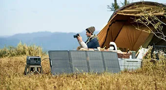 Mobil Solaranlage am Feld mit Solarpanelen, dahinter ein Mann mit Kamera neben einem Zelt
